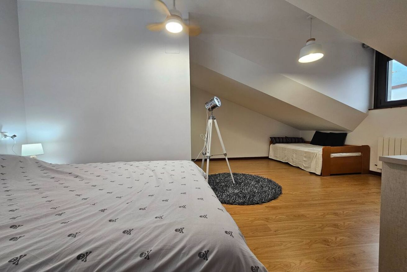Quarto moderno com uma cama grande, uma luminária de mesa, um tripé e um pequeno espaço de estar.