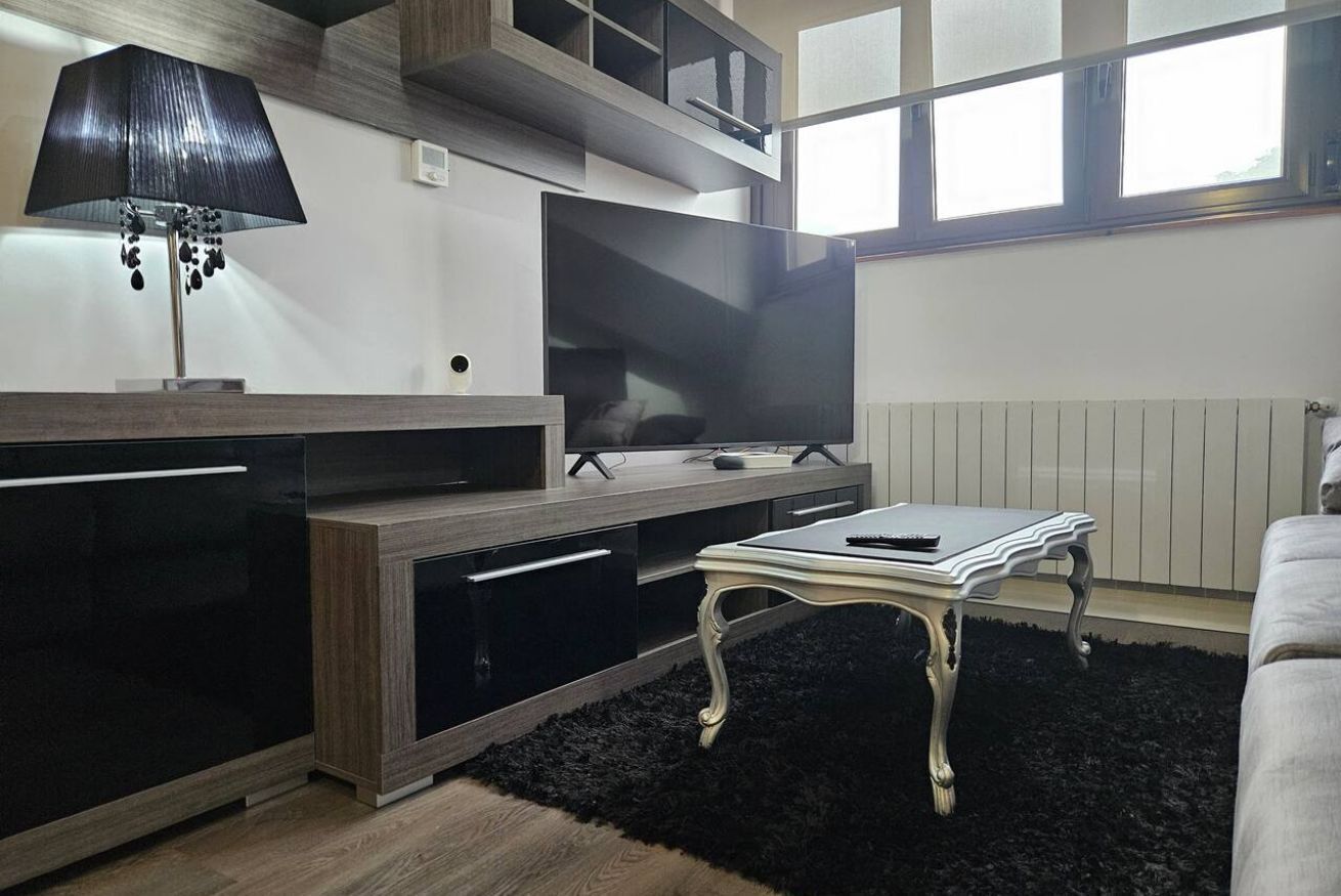 Uma sala de estar moderna com uma televisão de tela plana, uma luminária preta, uma mesa branca e um tapete preto.