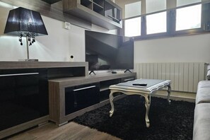 Un salon moderne avec un téléviseur à écran plat, une lampe noire, une table blanche et un tapis noir.