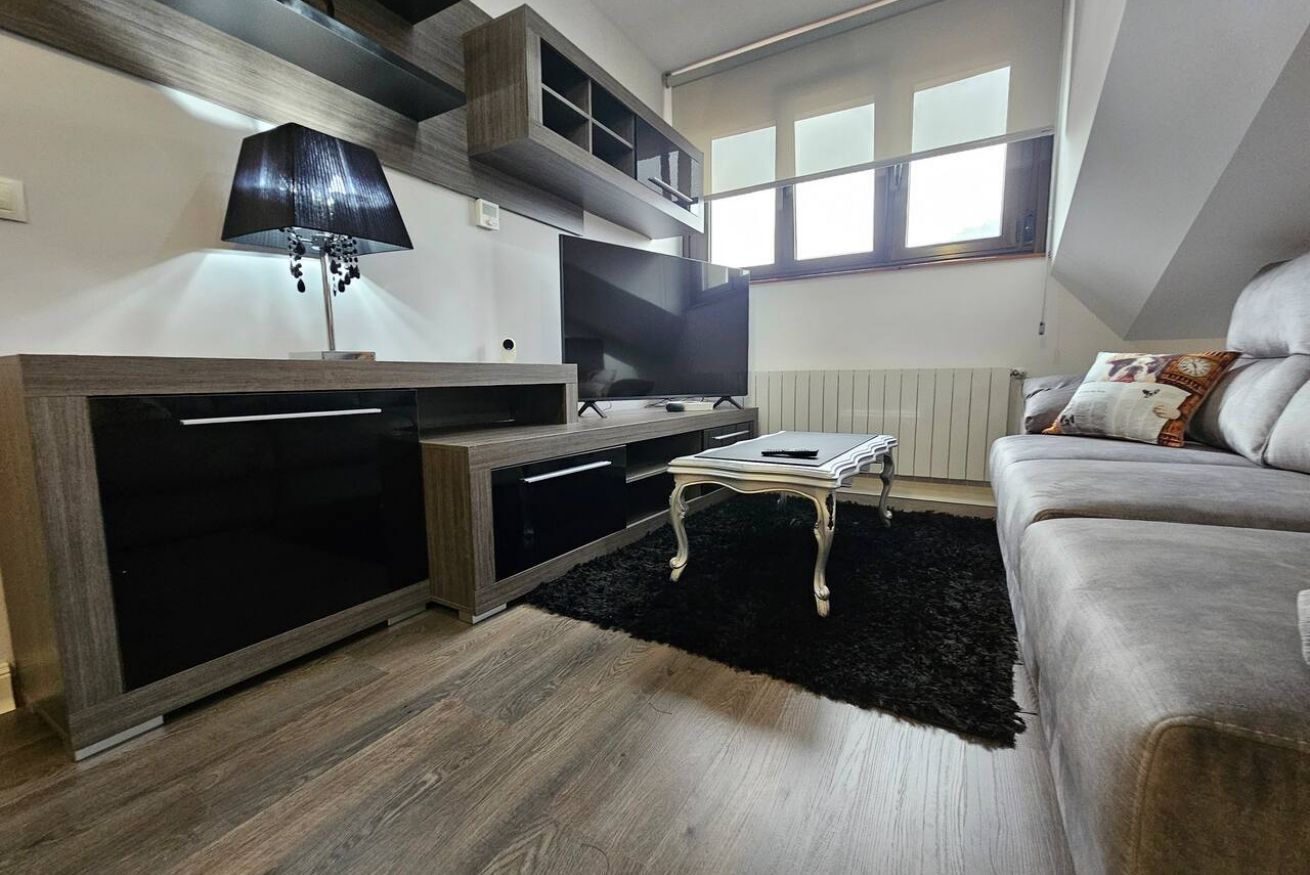 A modern living room with a TV, sofa, and a black rug.