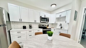 Una cocina moderna con armarios blancos, un microondas, una cafetera y una mesa de comedor con sillas.