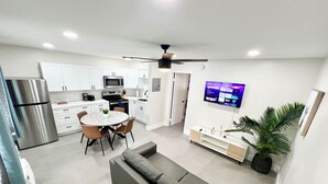 Una cocina moderna con armarios blancos, un refrigerador de acero inoxidable y una zona de comedor con una mesa redonda y sillas.