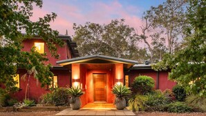 Una casa moderna con facciata rossa, porta d'ingresso in legno e un giardino curato con piante in vaso.