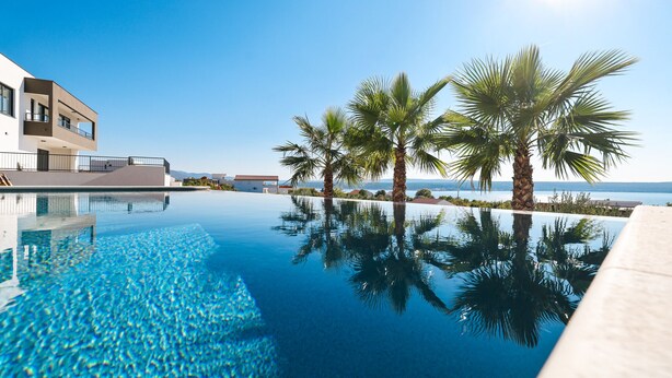 A modern hotel with a swimming pool, palm trees, and a view of the sea.