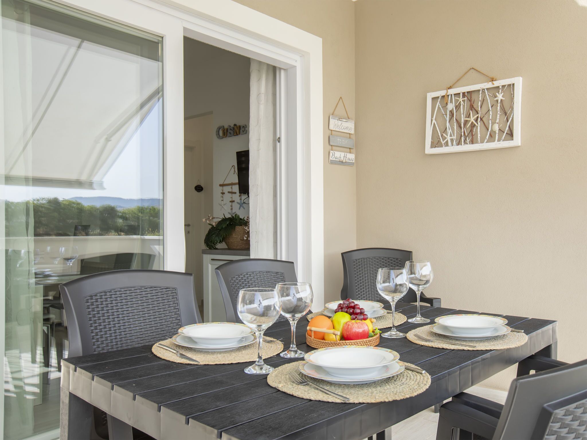 A dining table set with plates, glasses, and a fruit basket, with chairs around it.