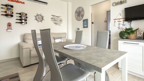 Un comedor moderno con una mesa gris, sillas grises, un sofá blanco y un televisor de pantalla plana montado en la pared.
