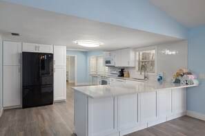 A modern kitchen with white cabinetry, a black refrigerator, and a central island. - Gorgeous Ranch Style Pool Home on One Acre Lot (Fort Myers)