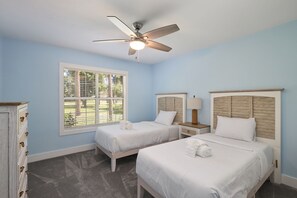 A bedroom with two beds, a ceiling fan, a window with blinds, and a dresser.