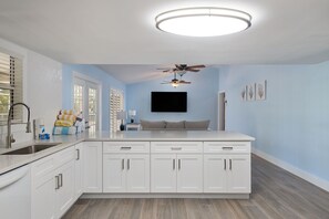 A modern kitchen with white cabinets, a central island, a ceiling fan, and a flat-screen TV mounted above the island.
