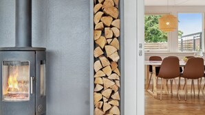Et moderne interiør med en brændeovn, et stabel med brænde og et spiseområde med stole og bord.