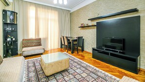 A living room with a sofa, ottoman, TV, and a dining area with chairs and a table. - Luxury Apartment with Flame Tower View (Baku)