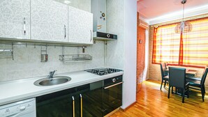 A modern kitchen with a built-in dishwasher, stove, and oven. There is a dining area with a table and chairs. - Luxury Apartment with Flame Tower View (Baku)