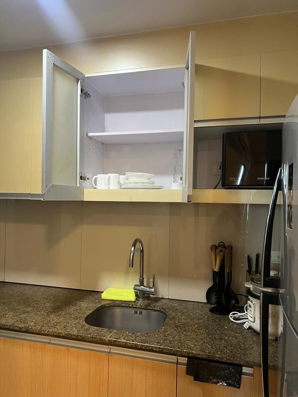 Una cocina con microondas integrado, un lavamanos de acero inoxidable y armarios de madera.