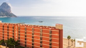 A hotel with a view of the ocean and a mountain in the background.