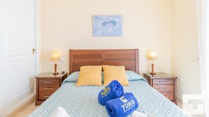 A hotel room with a wooden headboard, two bedside tables with lamps, a bed with patterned bedding, and two towels with 'TURIS' branding.