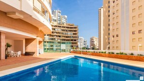 A swimming pool with a sun terrace, outdoor seating, and modern buildings in the background.