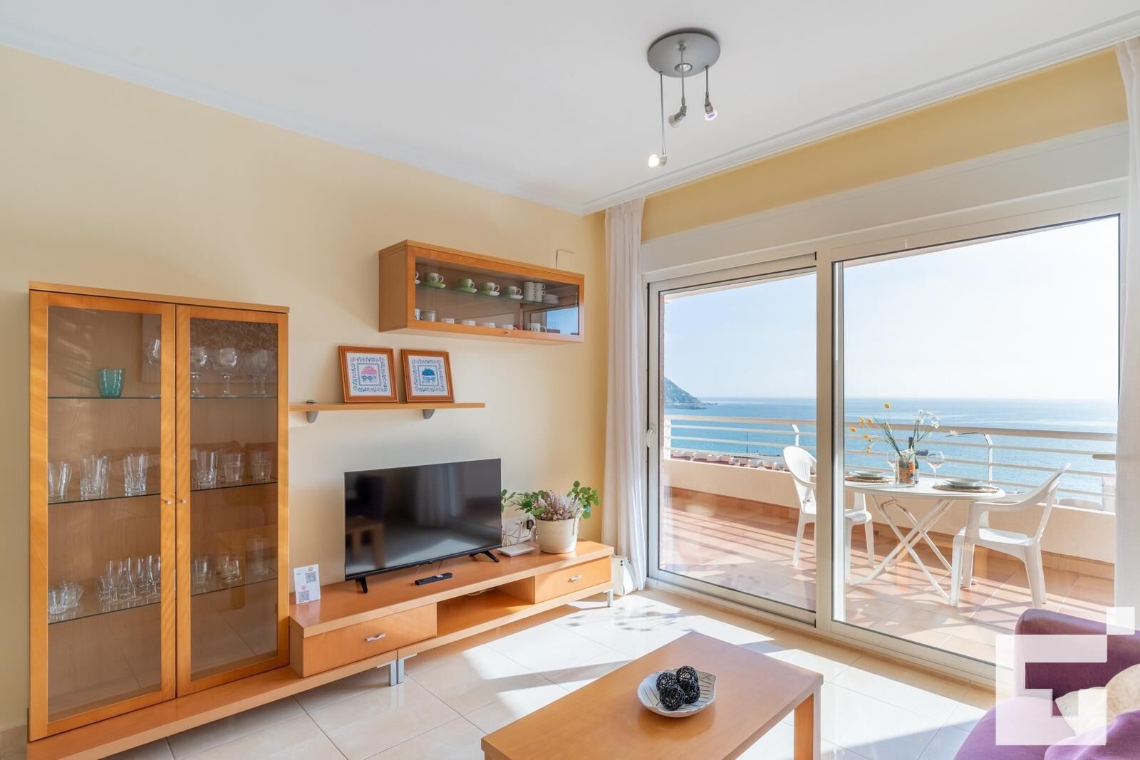 Amplia sala de estar con televisor grande, muebles de madera y balcón con vista al mar.