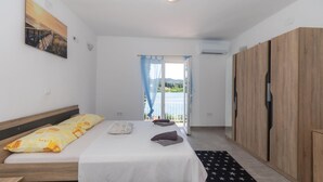 Un dormitorio con cama, armario, ventana con vista a un cuerpo de agua y un cuadro en la pared.