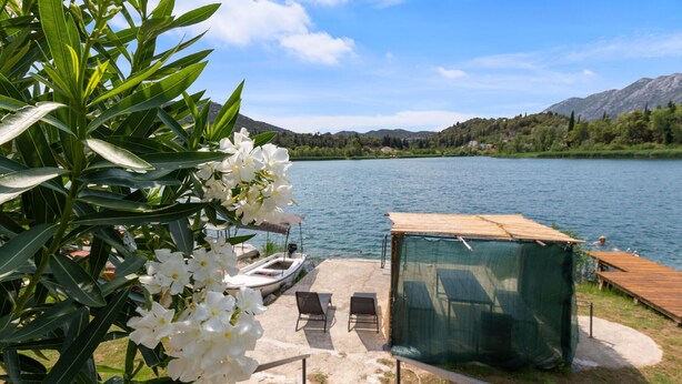 Un patio junto al lago con una pequeña zona de estar, un bote y una estructura cubierta.
