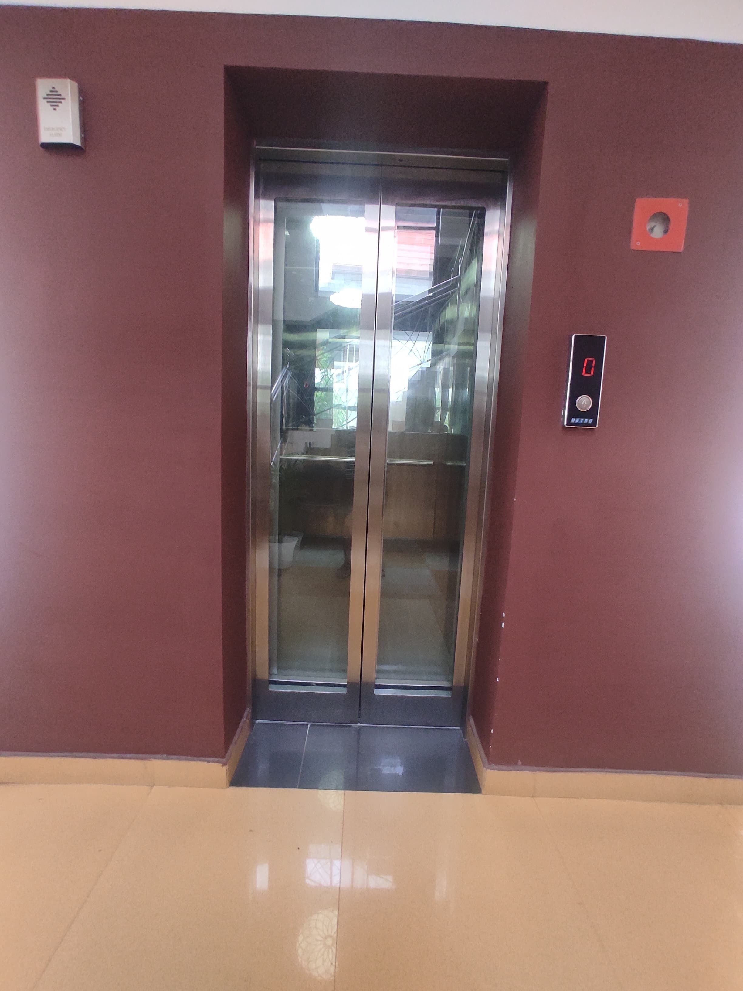 An elevator with a digital display, emergency button, and a red emergency exit sign on the wall.