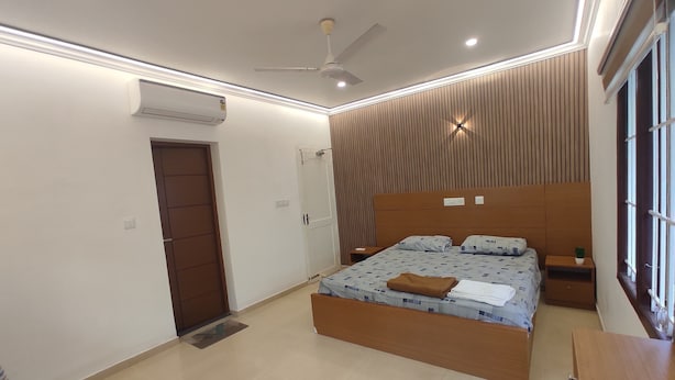 A modern bedroom with a large bed, a ceiling fan, an air conditioning unit, and a bedside table with a lamp.