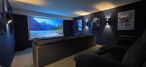 Une salle de cinéma privée avec un grand écran, des murs sombres et des affiches encadrées.