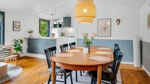 Een moderne keuken met witte paneelwanden, een eethoek met een houten tafel en stoelen, en een hanglamp.