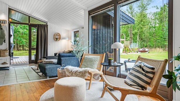 Een moderne woonkamer met een grote schuifpui die uitkomt op een terras, een bank, een salontafel en een rieten stoel.