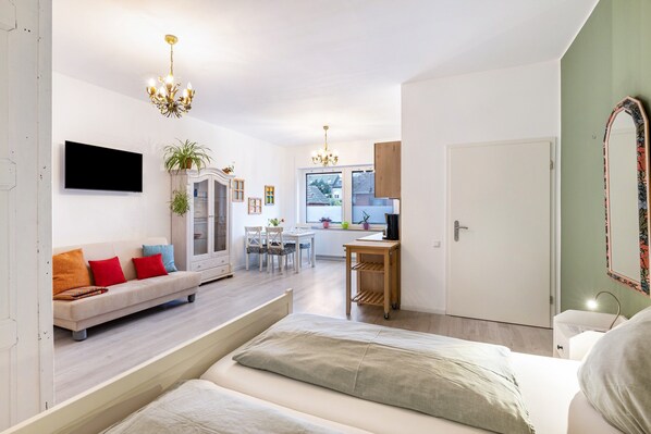 A modern living room with a sofa, a dining area, a kitchen, and a bedroom with a bed.