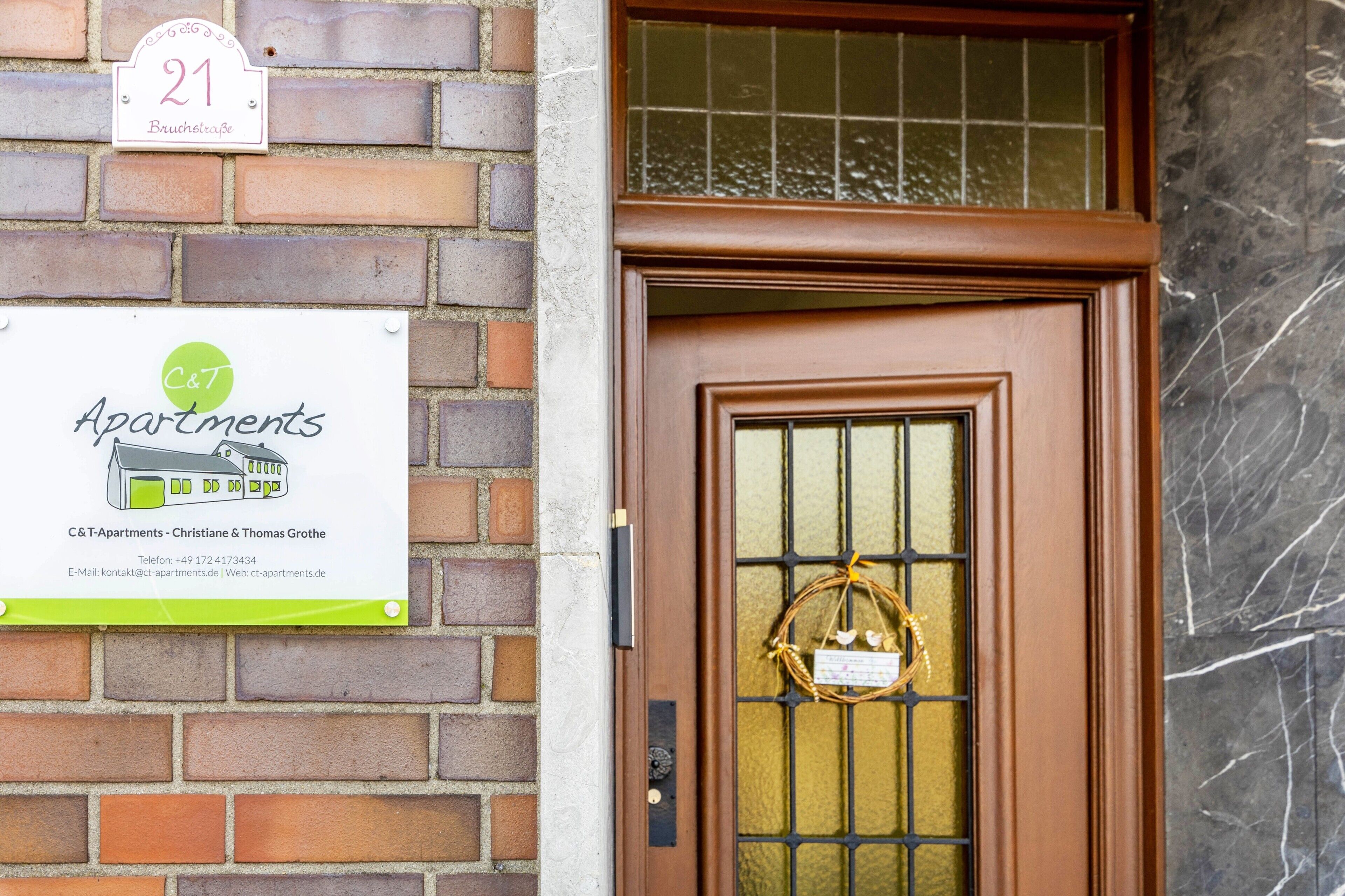 Een bakstenen muur met een bord voor C&T Apartments, een deur met een ruit en een gevel van baksteen.