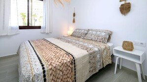 Un dormitorio con cama, mesita de noche, lámpara colgante y ventana con cortinas.