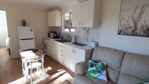 A modern kitchen with white cabinets, a dining area with a white table and chairs, and a beige sofa with a plant pillow.