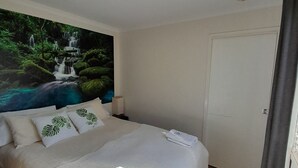 A bedroom with a bed, a nightstand, a wall-mounted light, a door, and a large window.