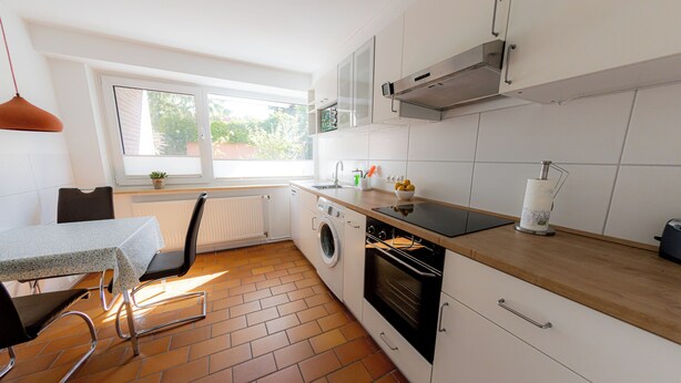 Una cocina moderna con lavadora, horno y comedor con mesa y sillas.