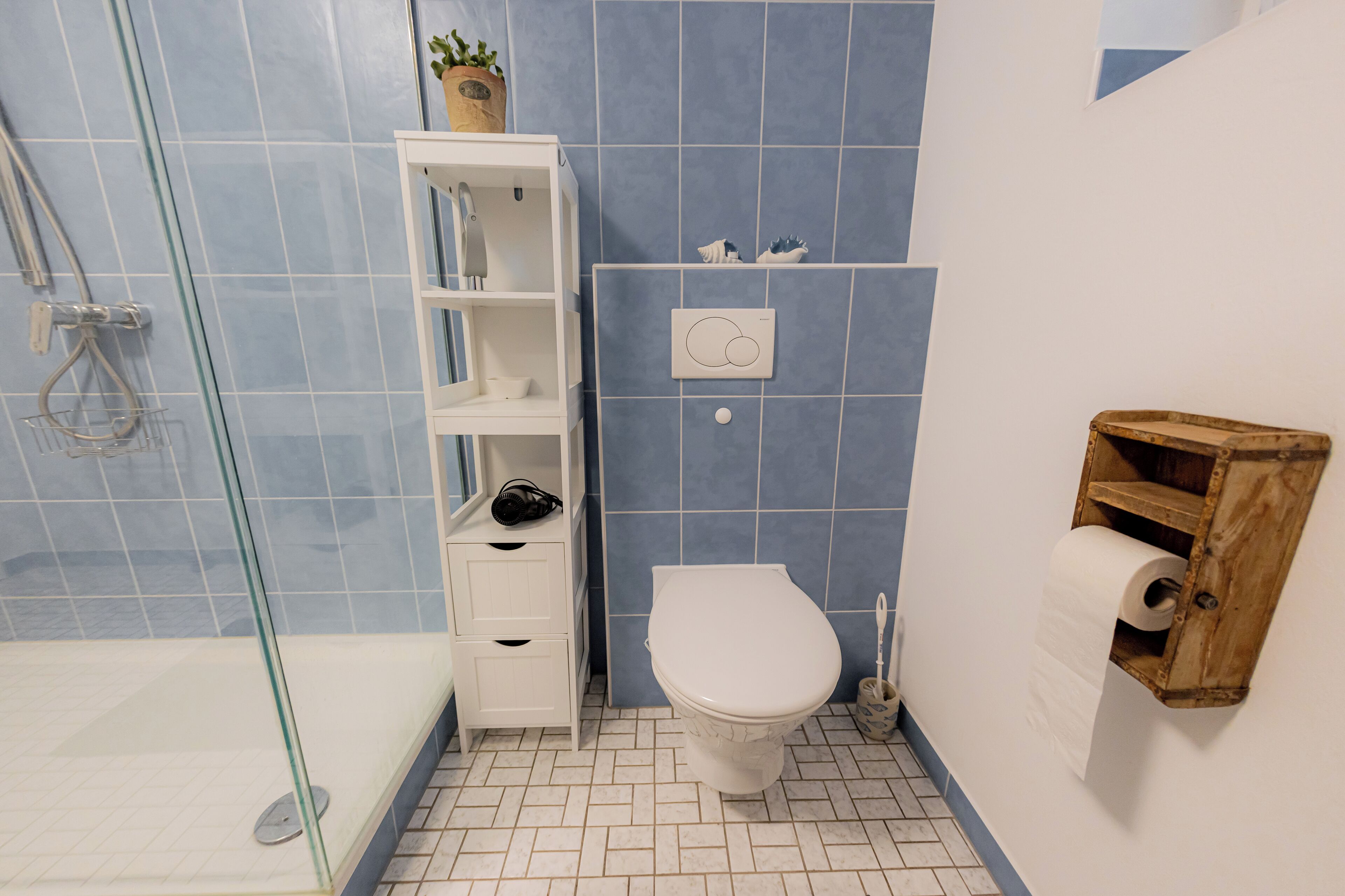 Un baño con ducha, inodoro y un estante con artículos de aseo.