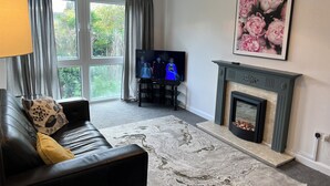 Ein Wohnzimmer mit einer schwarzen Ledersofa, einem Kamin, einem Fernseher und einem großen Fenster mit Vorhängen.