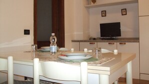 Un comedor con una mesa dispuesta para dos personas, un televisor en la pared y un estante pequeño con una planta.