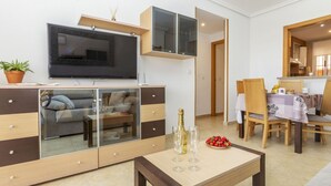 Ett modernt vardagsrum med en platt-TV, ett soffbord med glasskiva och en matplats med trästolar och ett bord.