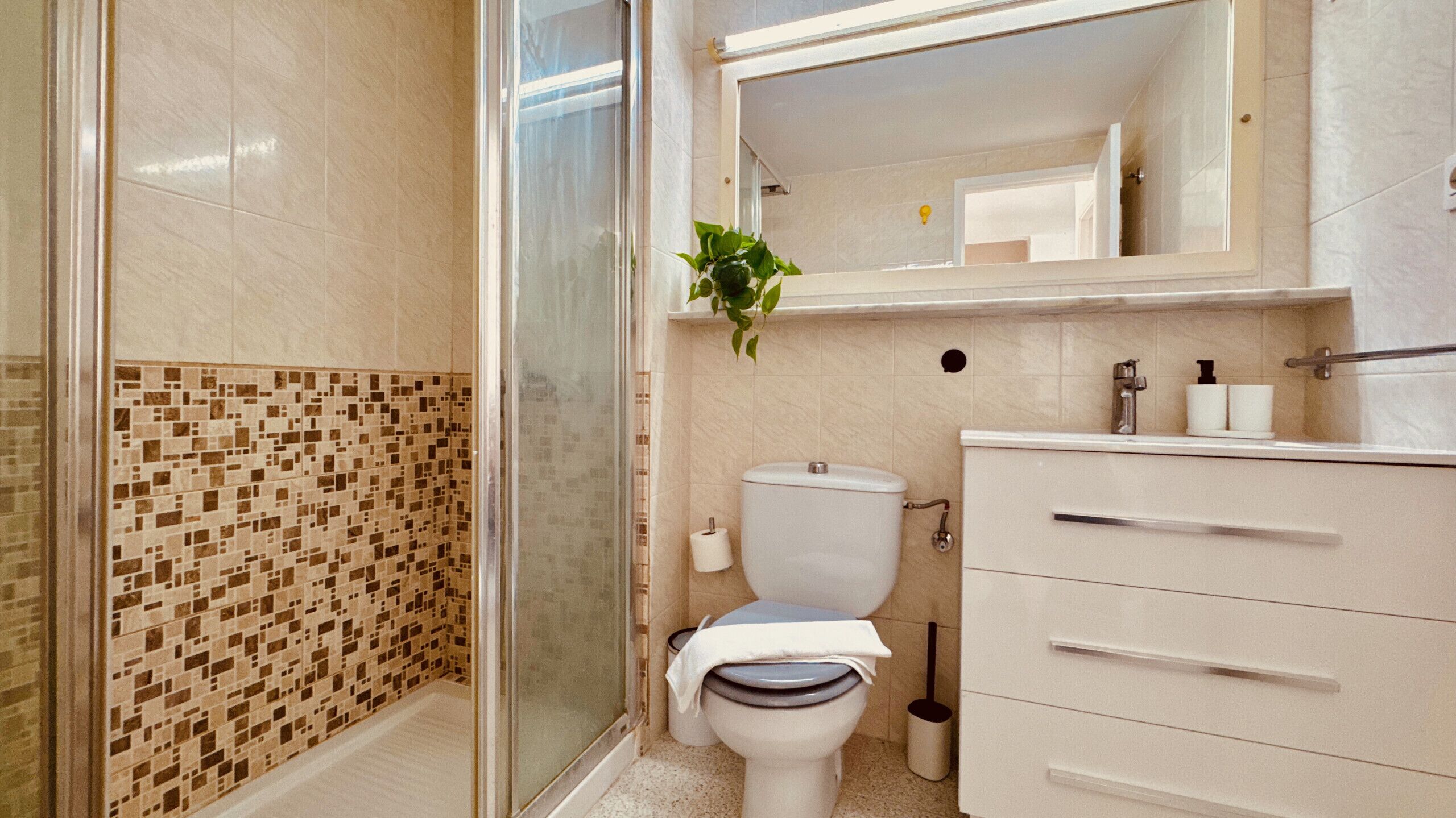 A bathroom with a shower, toilet, sink, and mirror.