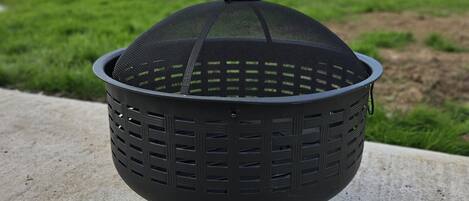 Een zwarte buitenbarbecue met een gaas bovenkant, op een betonnen oppervlak, met een grasveld op de achtergrond.
