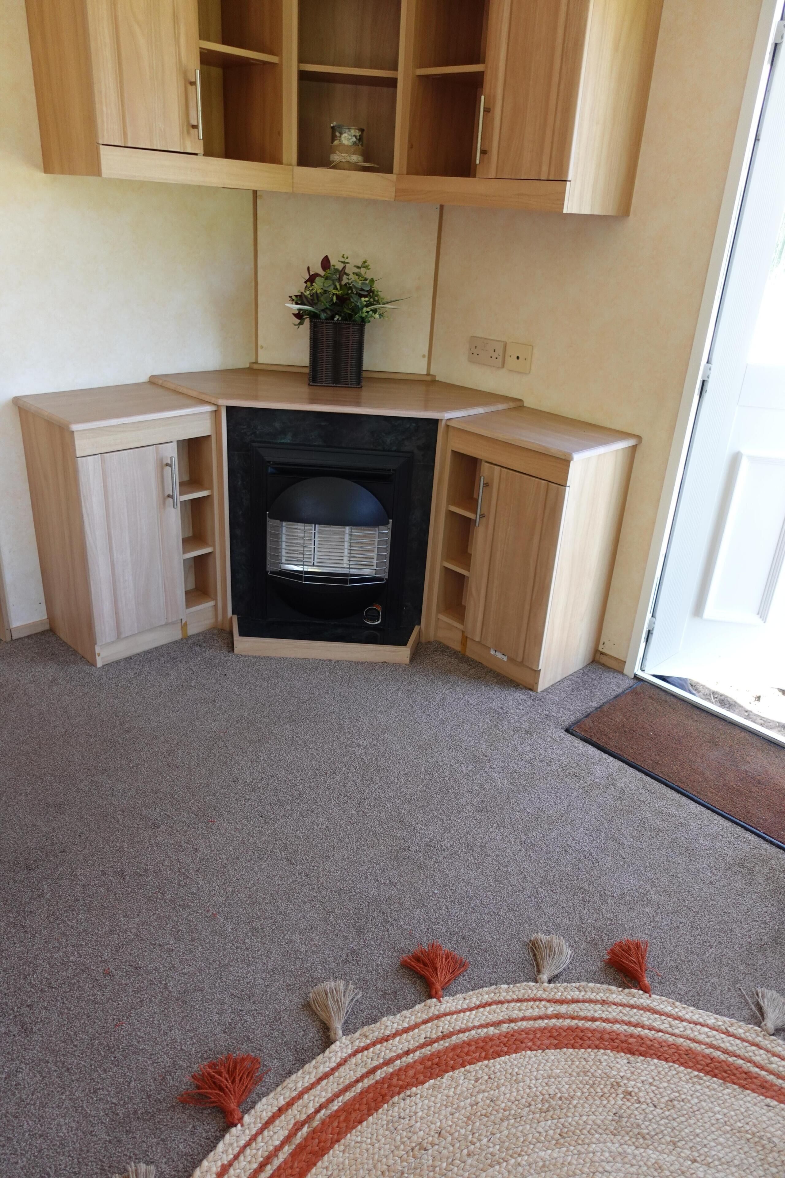 A corner room with a fireplace, wooden cabinets, a potted plant, and a doormat.