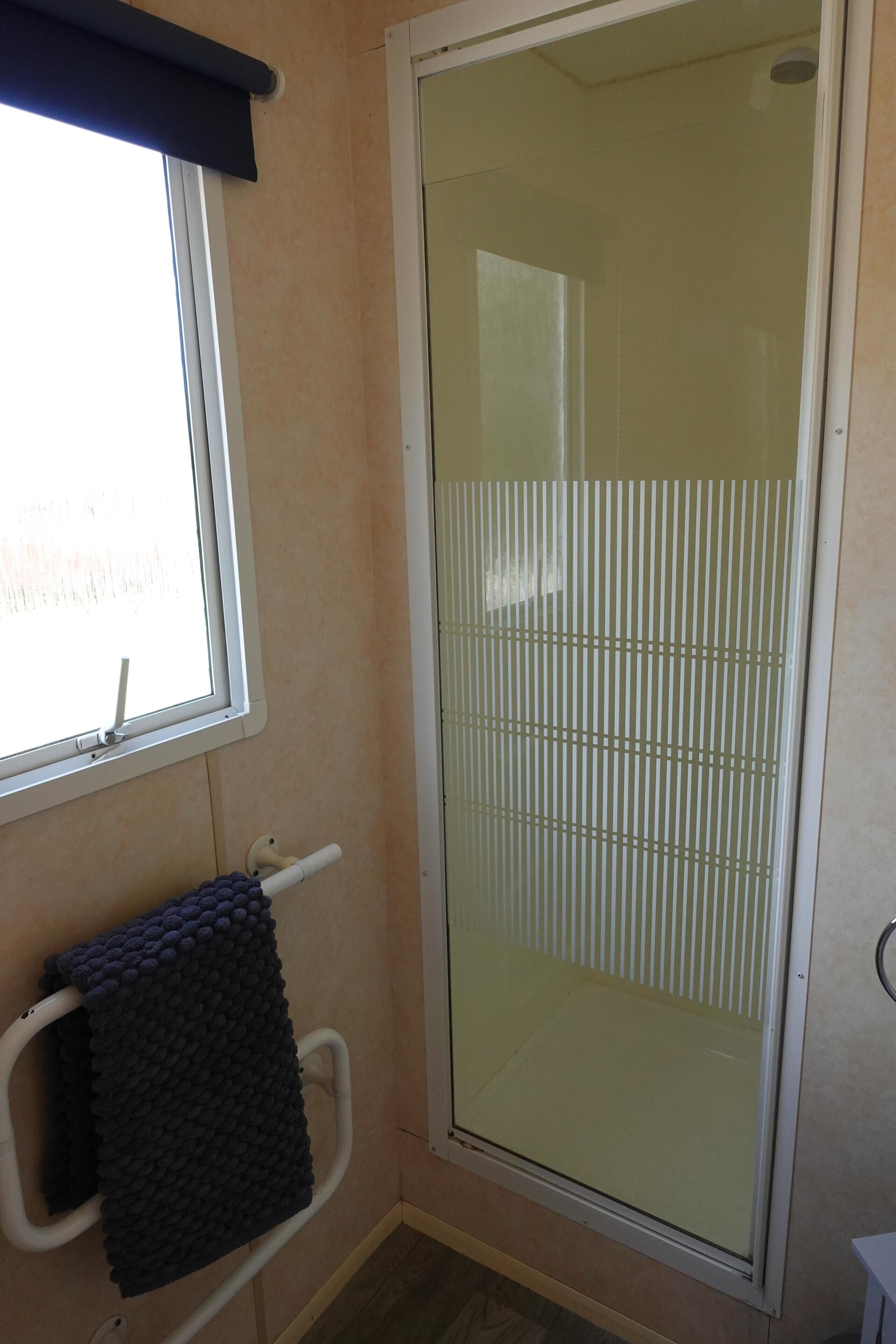A bathroom with a glass shower enclosure, a towel rack with a dark towel, and a window with a white frame.