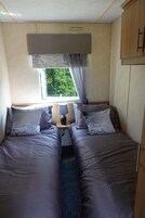 Un dormitorio compacto con dos camas, una ventana con cortinas, una lámpara y un armario.