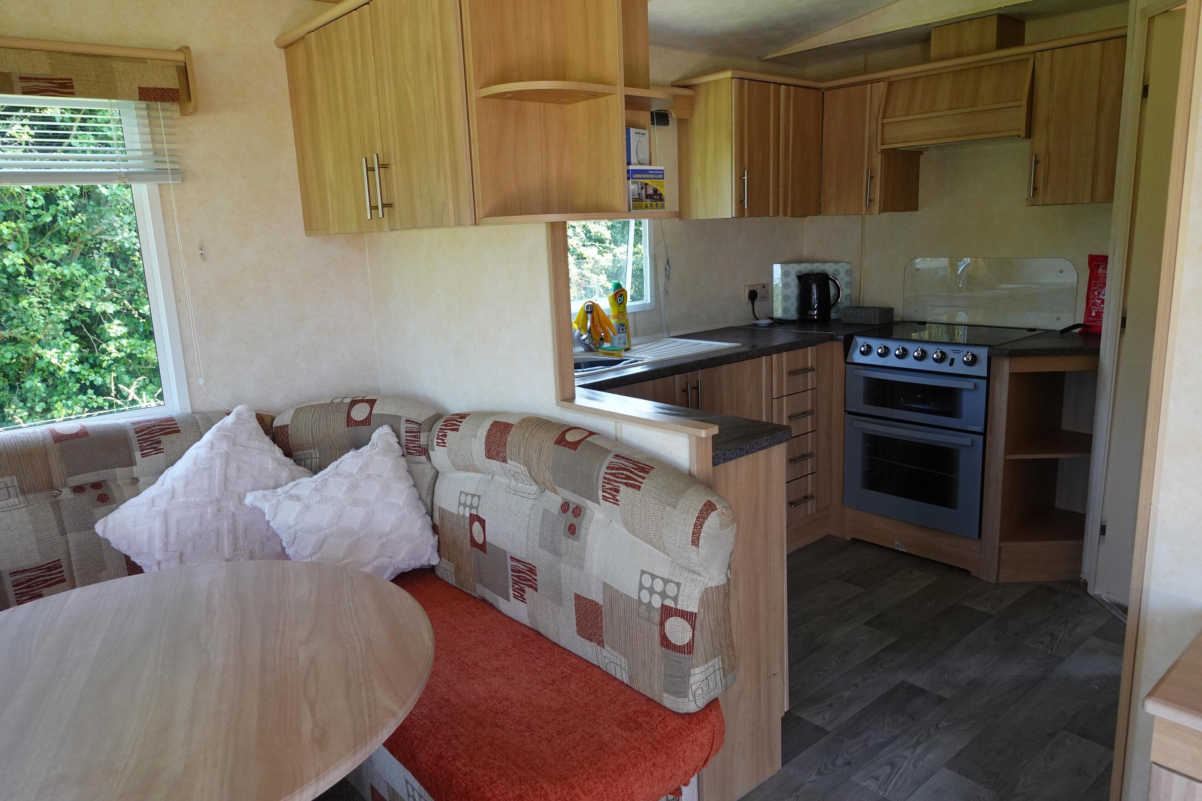 A compact kitchen with wooden cabinets, a stove, and a dining area with a sofa and table.