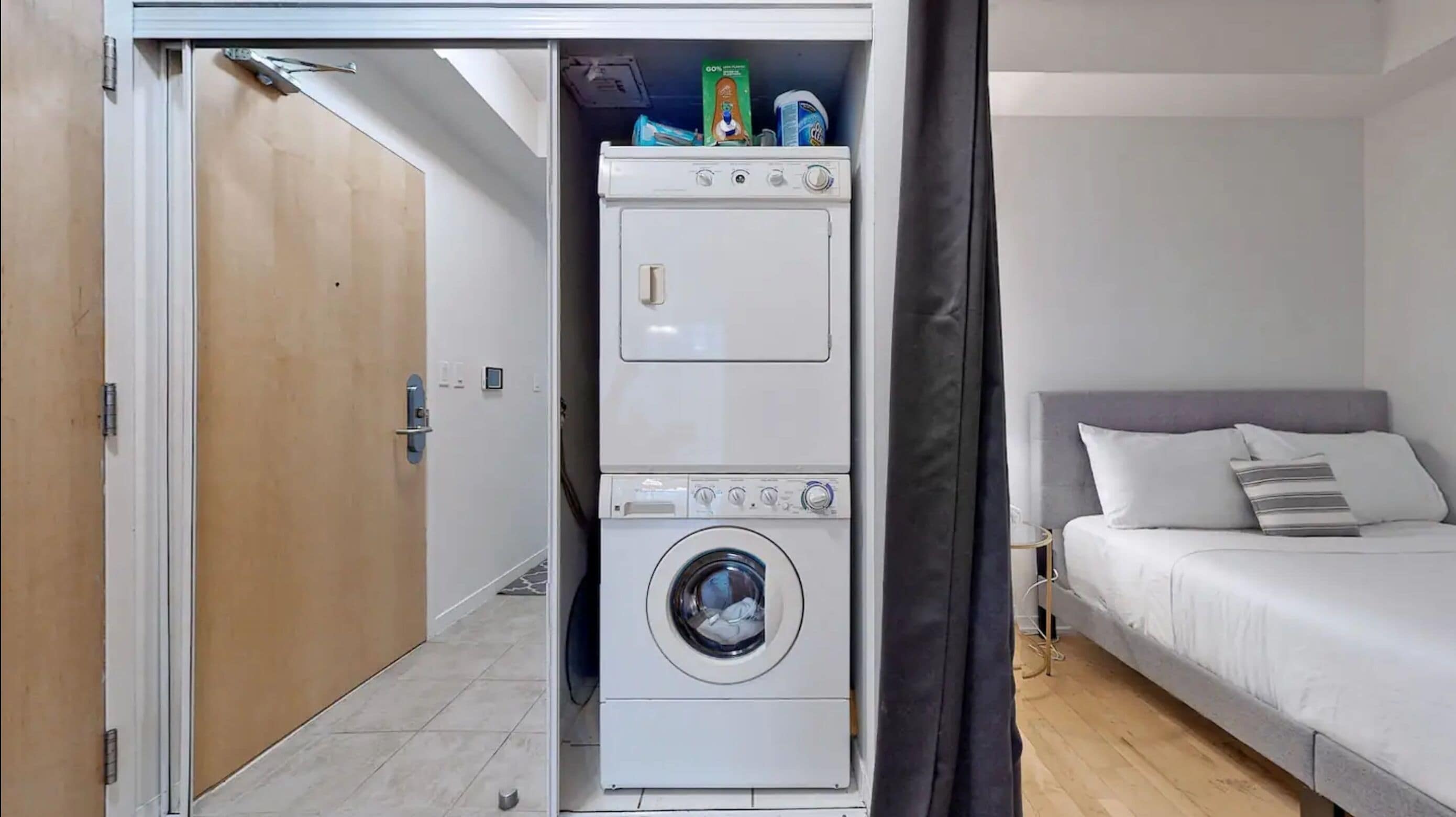 Habitación pequeña con lavadora, cama y puerta que da a otro espacio.