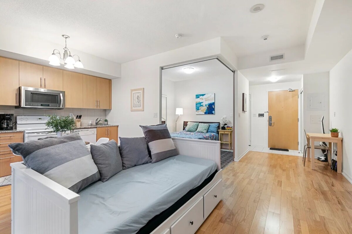 A compact living space with a kitchenette, a sofa bed, a dining area, and a door leading to another room.