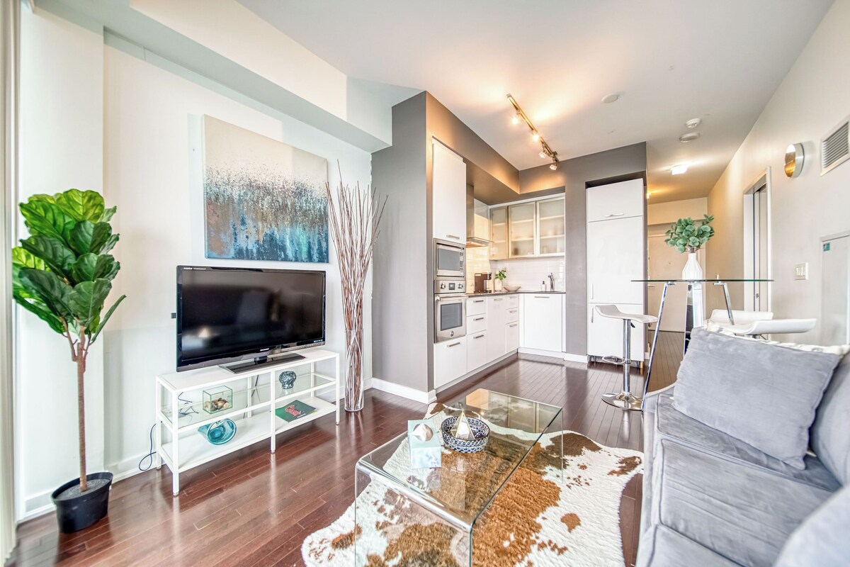 A modern living room with a flat-screen TV, a glass coffee table, and a grey sofa.