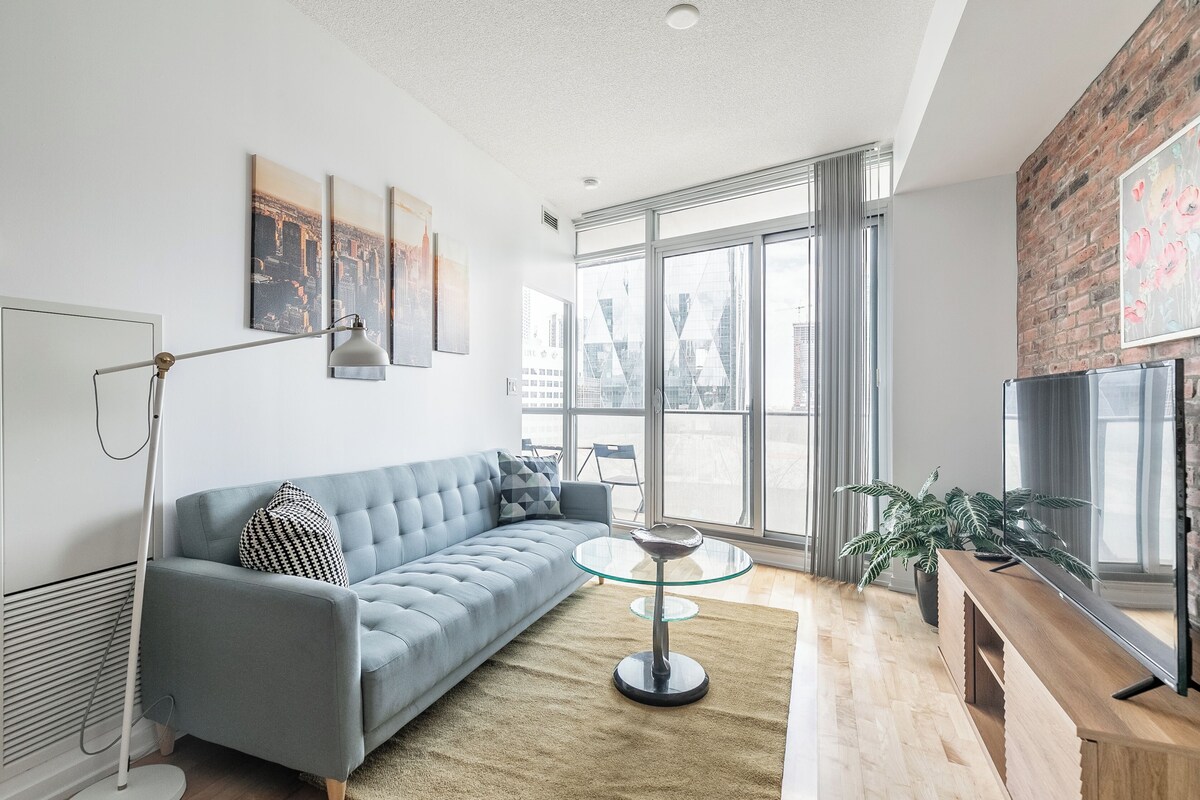 A modern living room with a grey sofa, a glass coffee table, and a TV on a wooden stand.