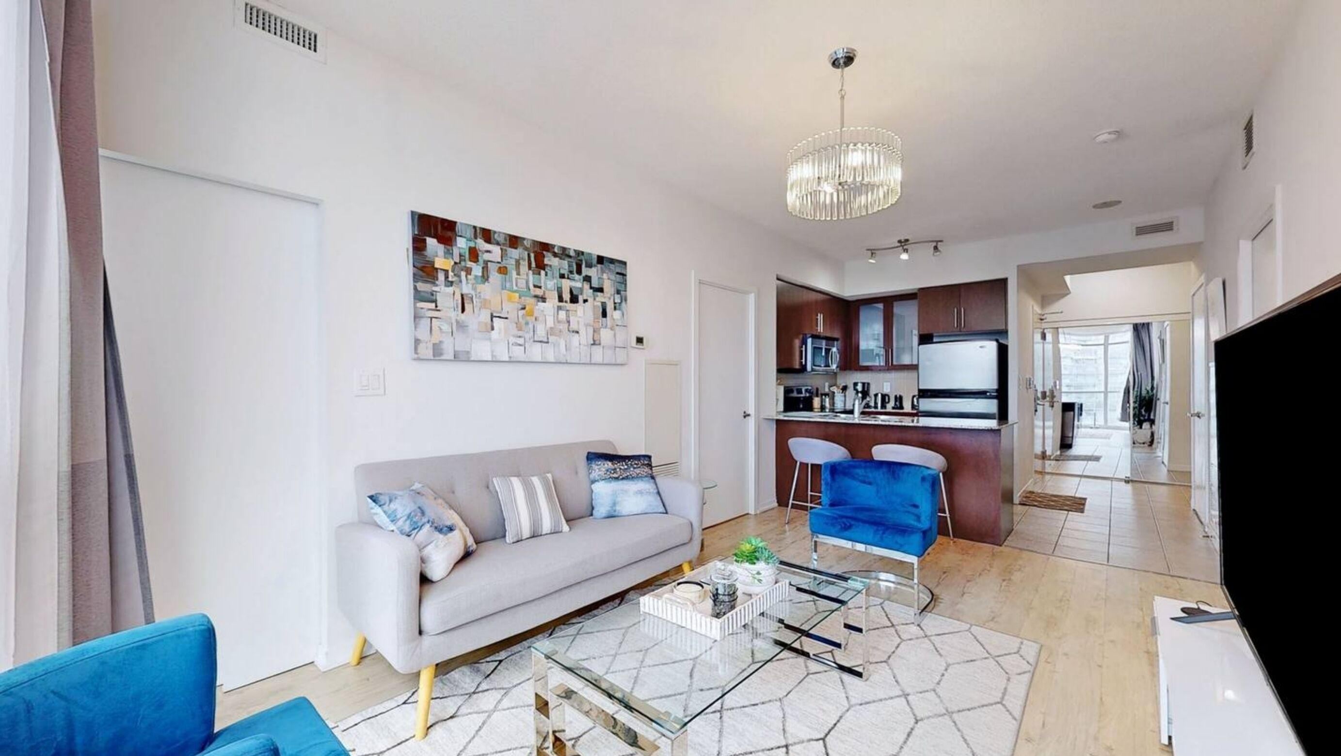 Ein modernes Wohnzimmer mit einem grauen Sofa, blauen Sesseln, einem Glastisch und einer Chandelier.