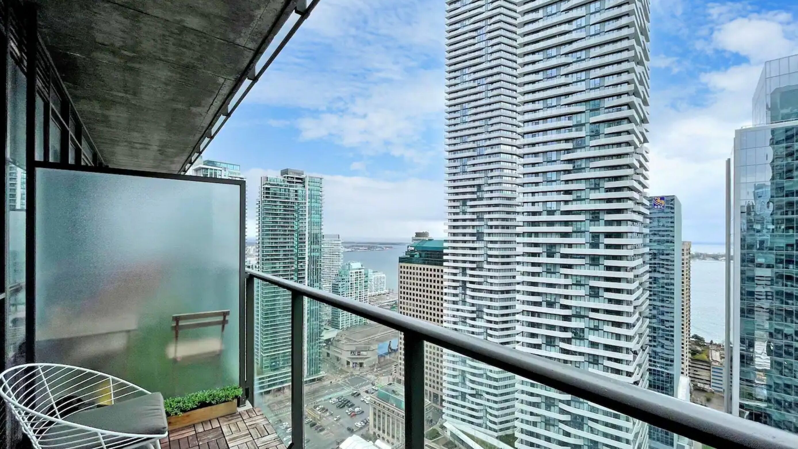 Un edificio alto con fachada de vidrio, un balcón con una silla blanca y vistas a la ciudad y al agua.